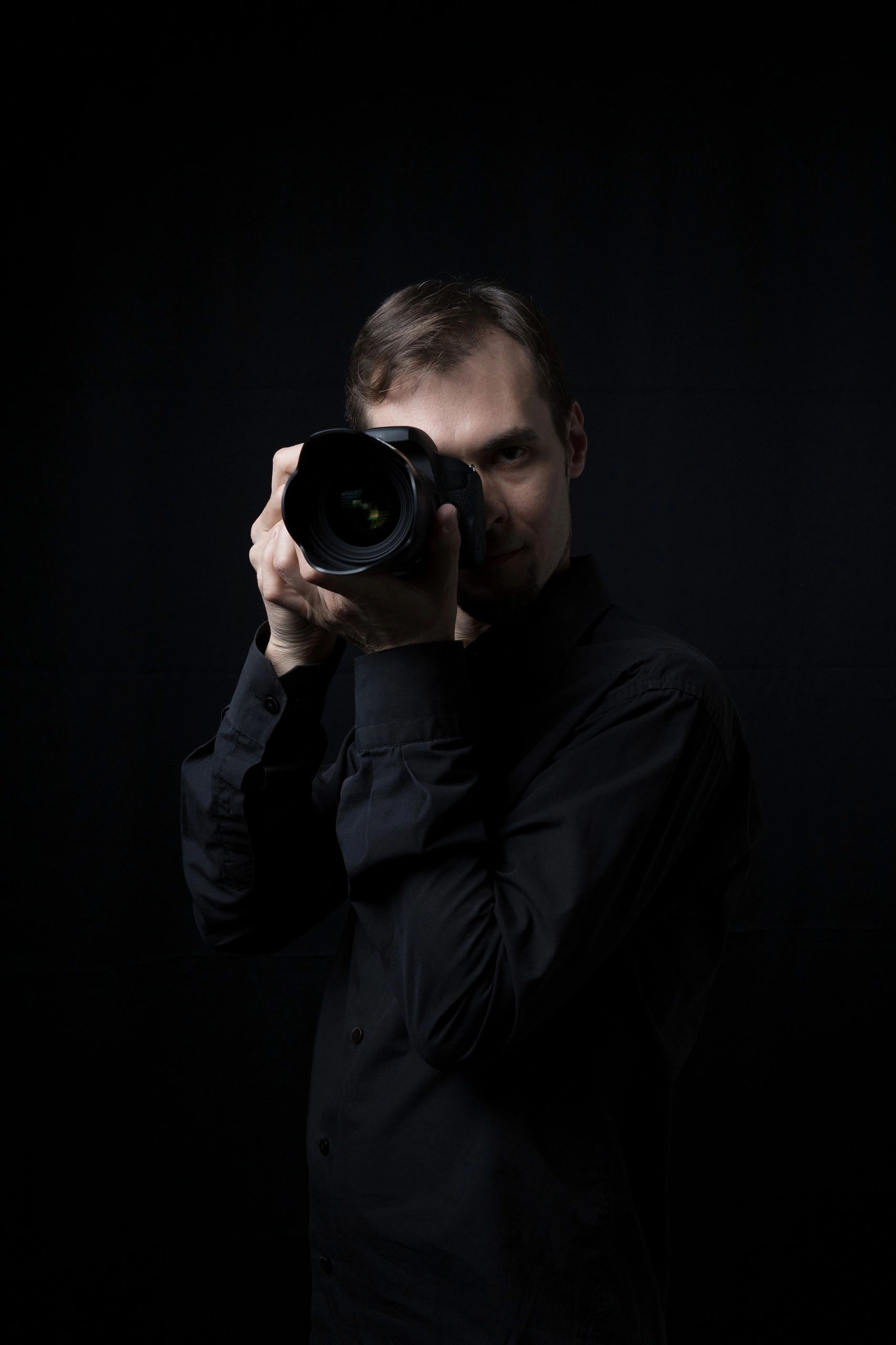 Low key portrait of a photographer holding a camera in a dark studio