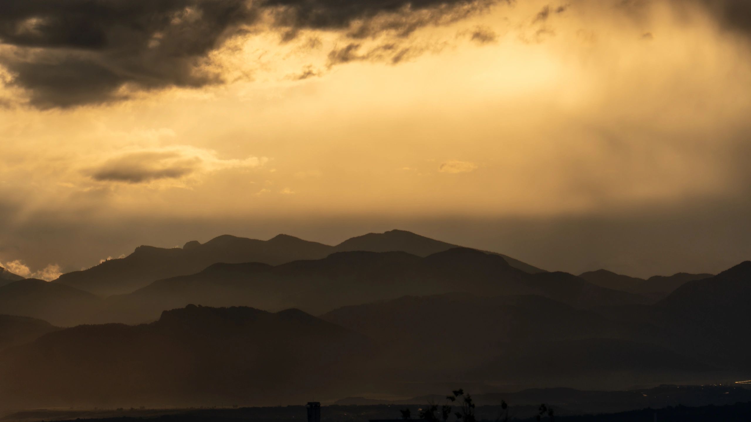 Sunset rays breaking through storm clouds over mountain silhouettes