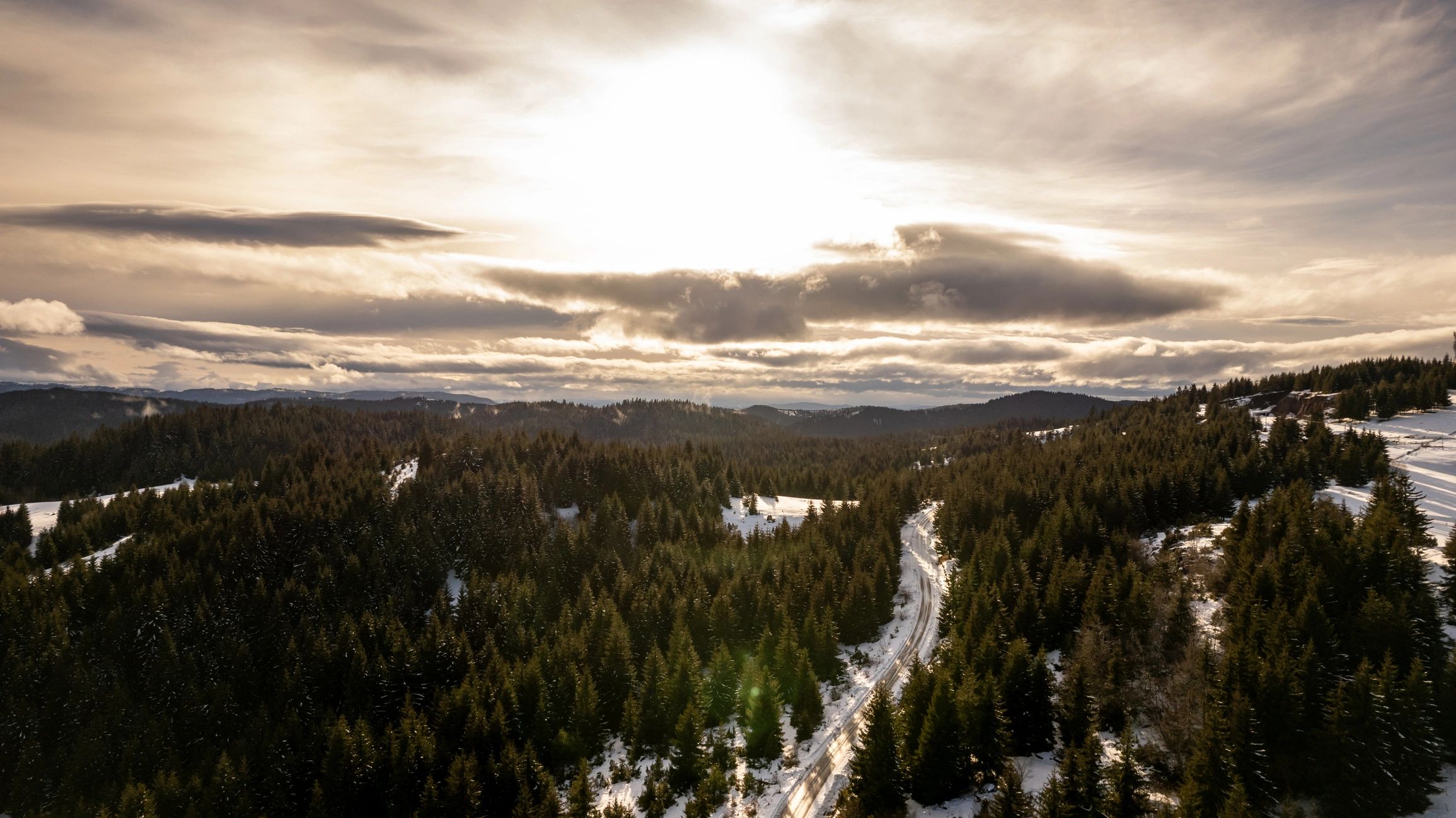 Winter forest road winding through snowy mountain landscape
